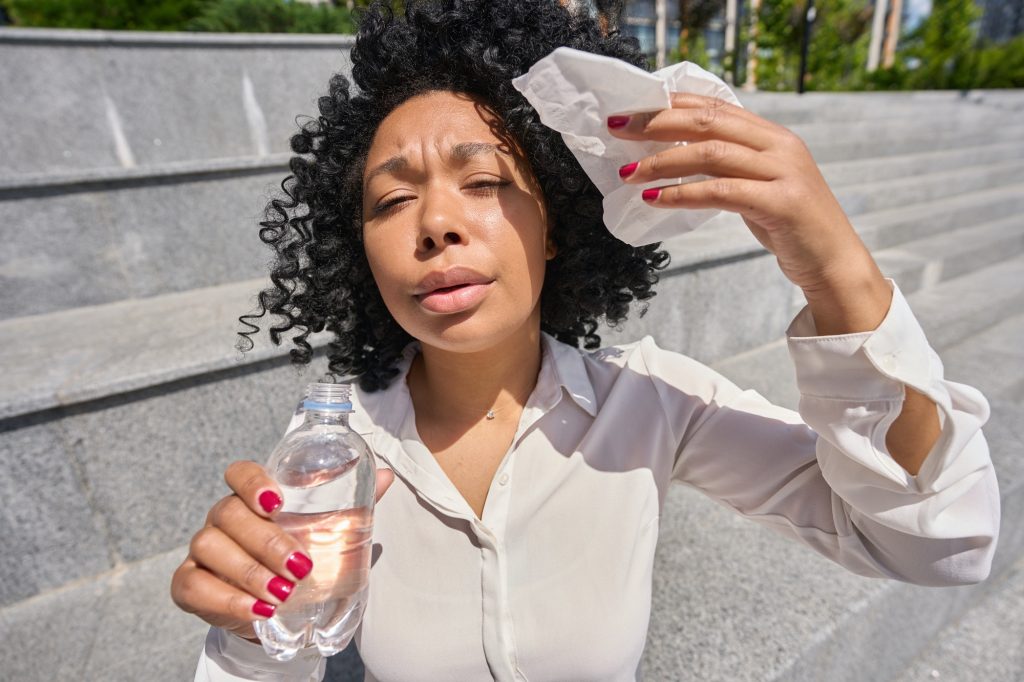 Mujer multirracial sentada en el calor limpiándose con una servilleta y bebiendo agua